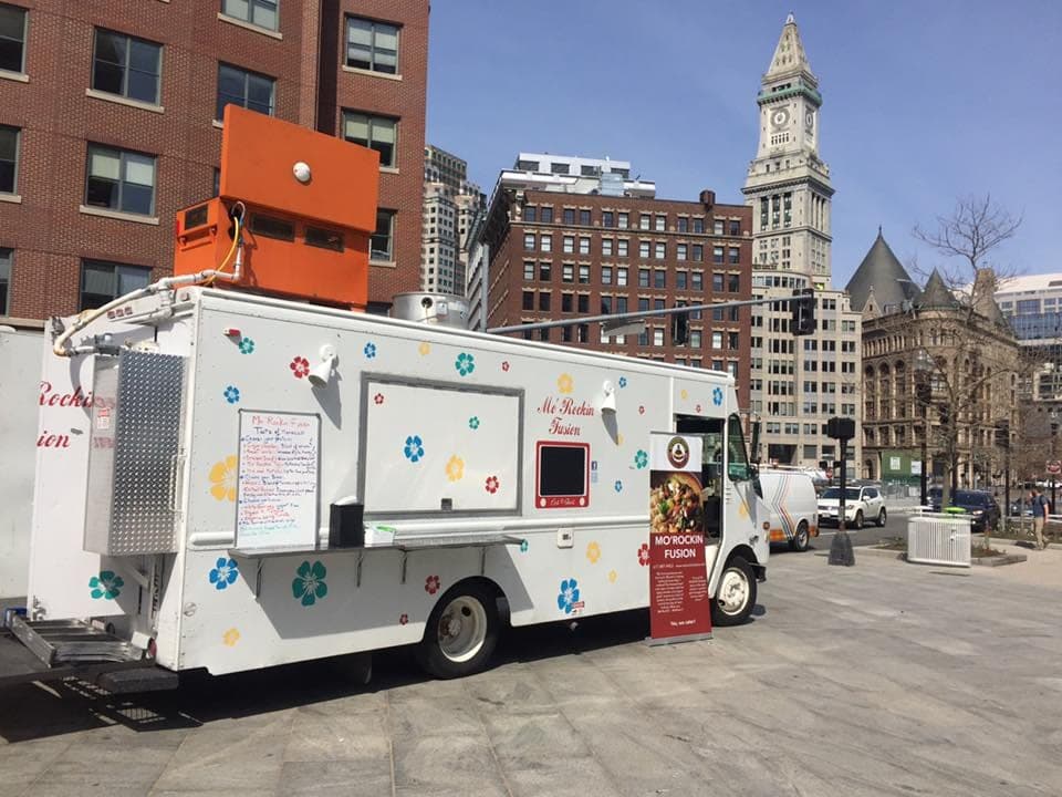 A white food truck parked on a Boston street with the old Custom House tower behind it