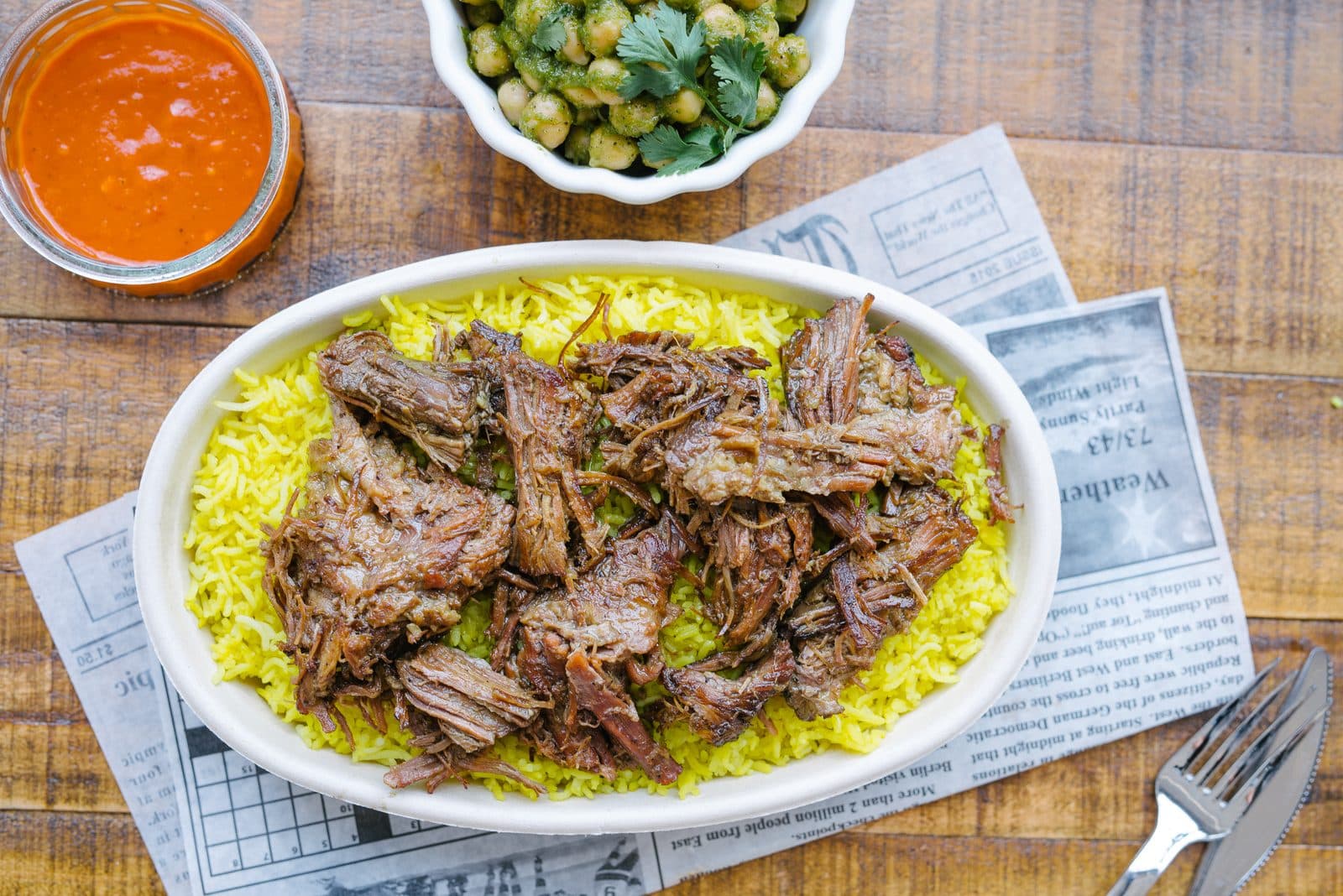 Slow cooked beef over yellow rice with a bowl of red sauce and a bowl of olives