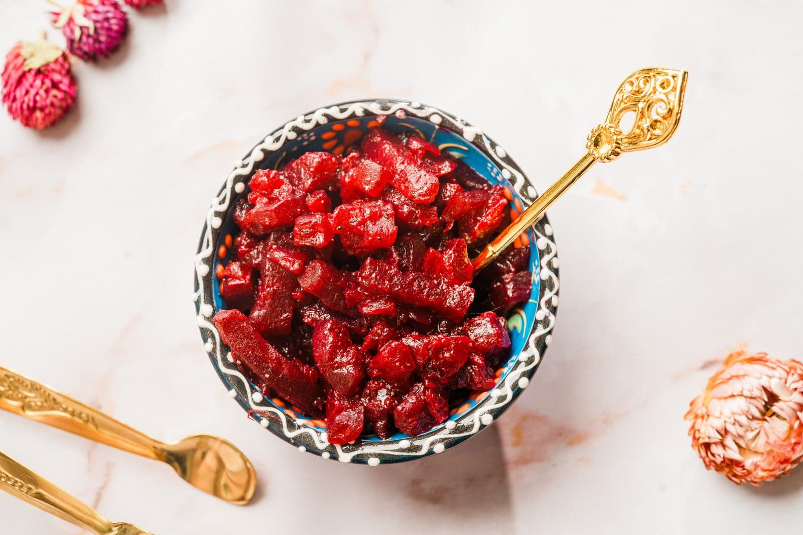 A bowl of diced beets with a gold serving spoon on a marble surface