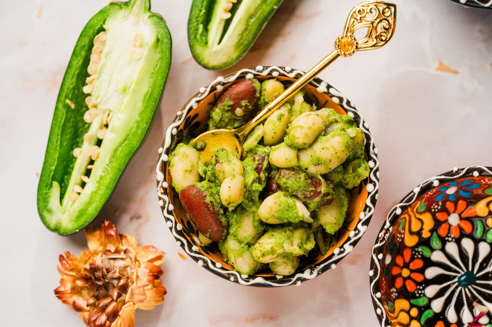 A bowl of beans with roasted peppers and herbs, next to a halved jalapeño