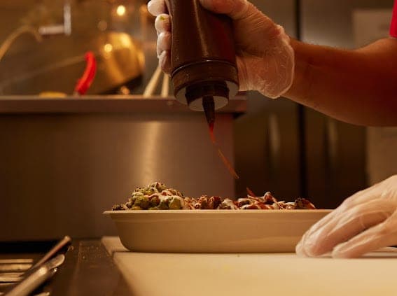 A bowl being finished with sauce from a squeeze bottle behind the counter