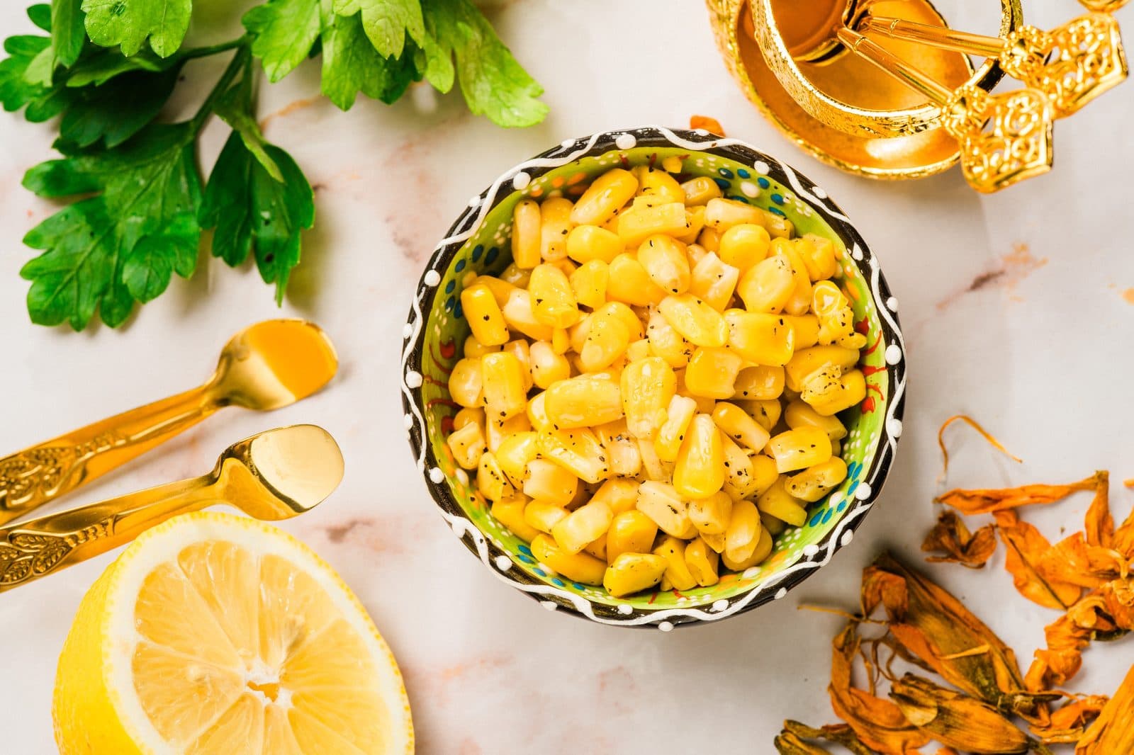 A bowl of sweet corn with lemon and herbs on a marble surface