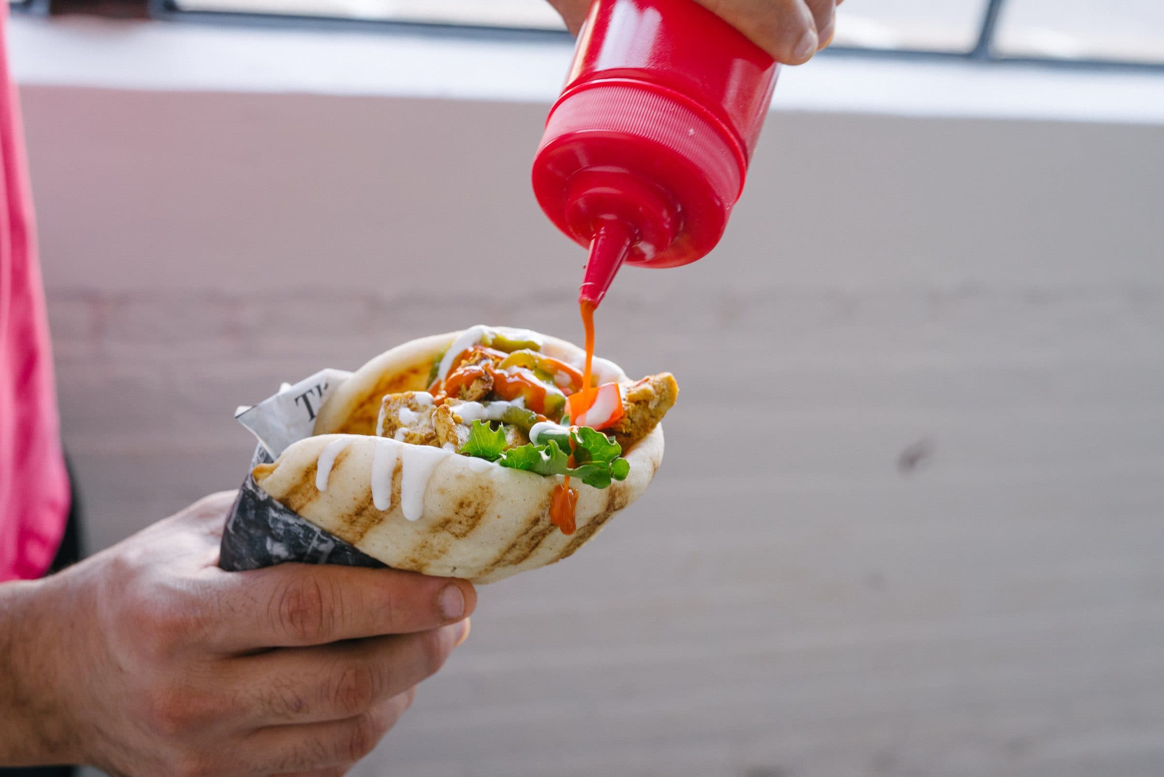 A hand finishing a filled flatbread with sauce from a squeeze bottle