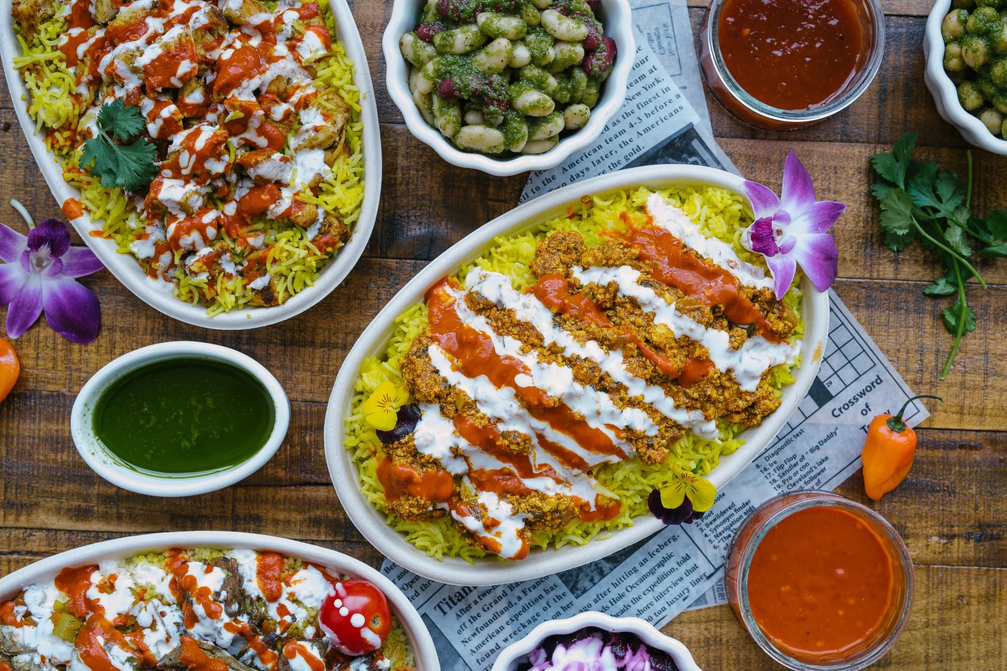 Several oval dishes of yellow rice finished with red and white sauce, with bowls of sauce and sides on a wooden table
