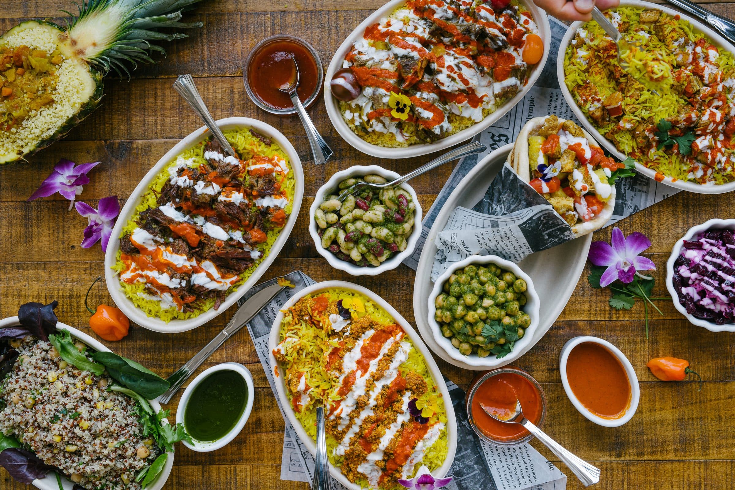 A wooden table laid with oval dishes, small bowls of sides and sauces, photographed from above