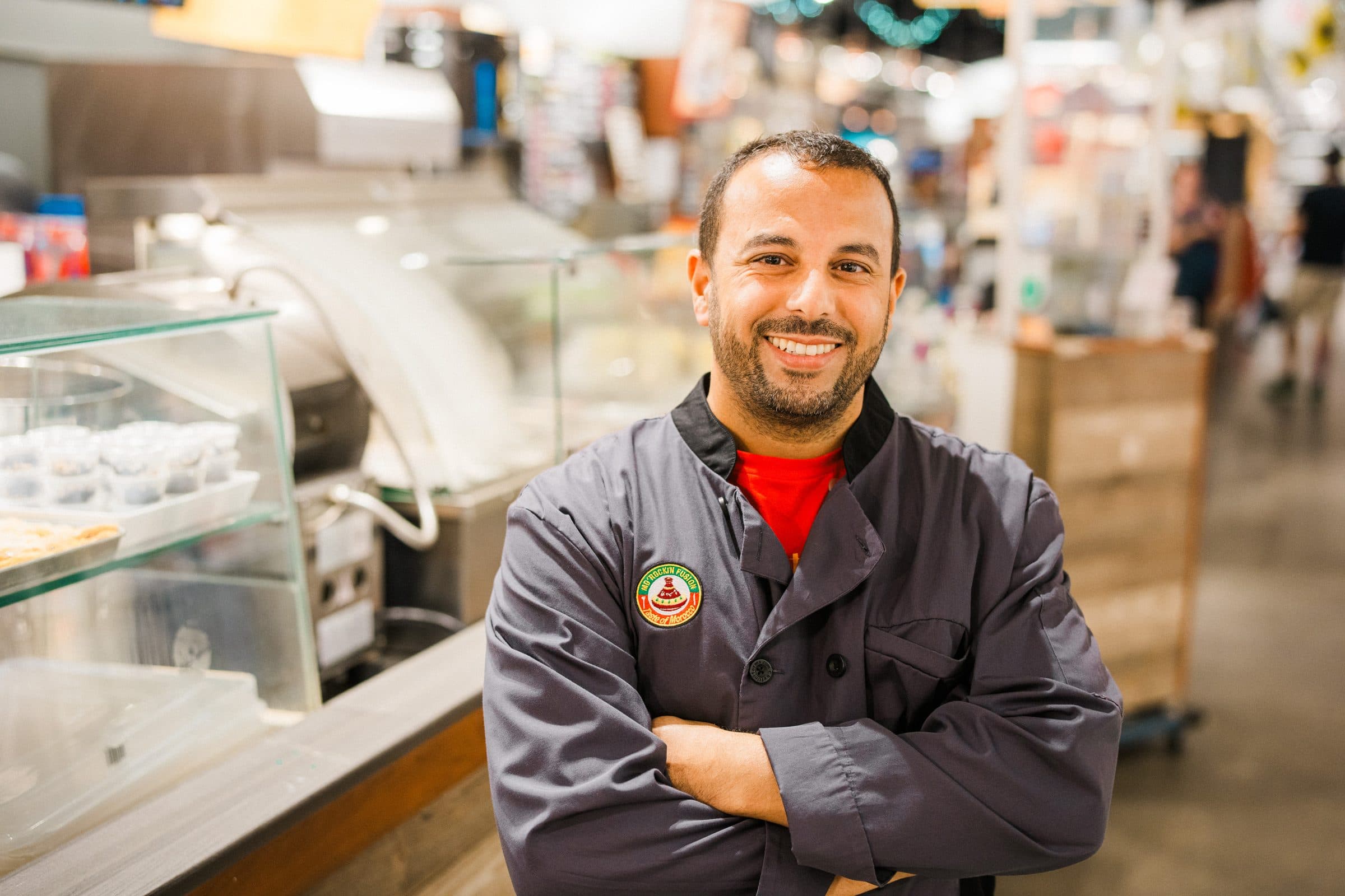 A chef in a Mo'Rockin Fusion jacket standing at the stall inside Boston Public Market