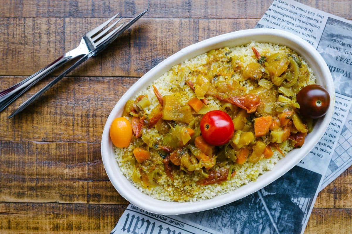 Couscous with roasted vegetables and cherry tomatoes on an oval dish, on a wooden table